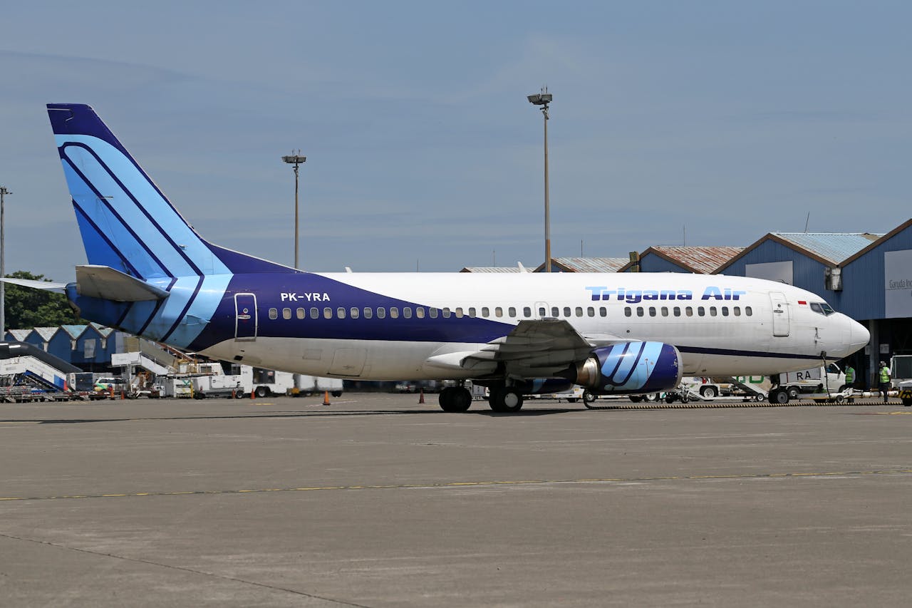 contact-img Side view of a Trigana Air aircraft parked on an airport apron under a clear sky.