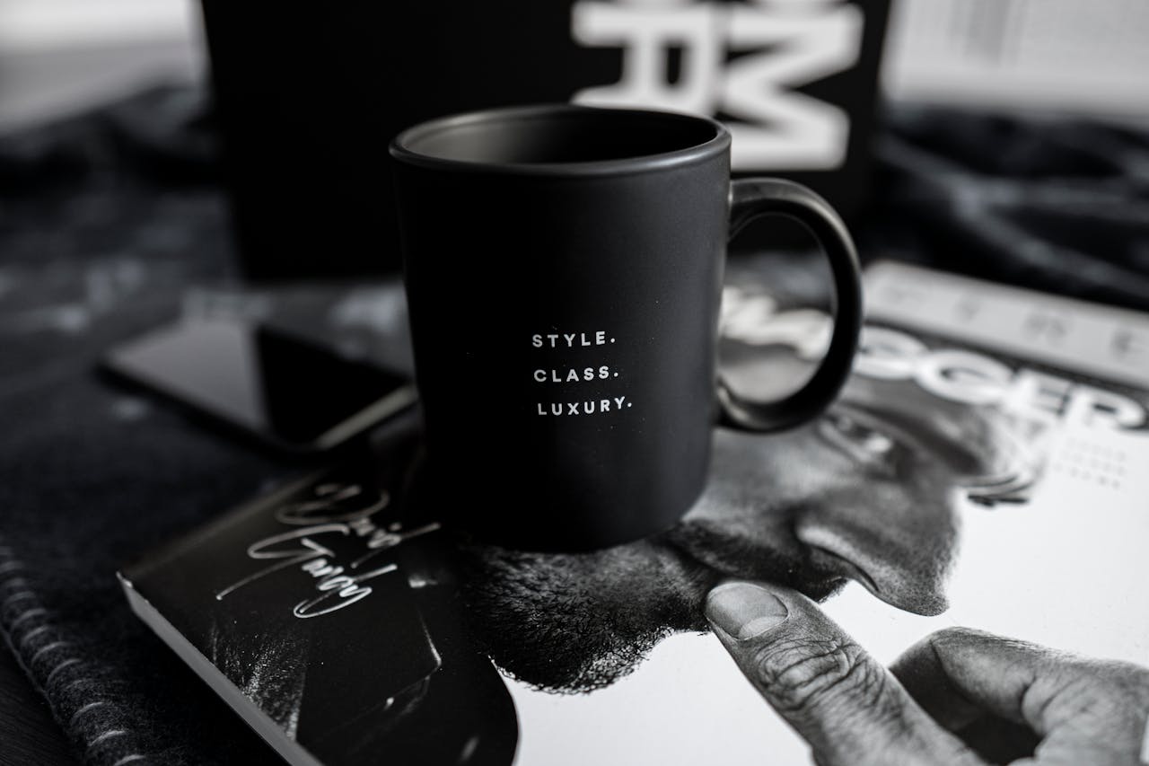 home-img A stylish black mug with text sits on a luxury magazine, presenting an elegant and modern lifestyle setting indoors.